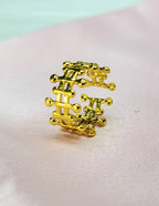 Celestia adjustable tarnish-free gold plated stainless steel crown ring with intricate architectural beadwork displayed on a soft pink background.