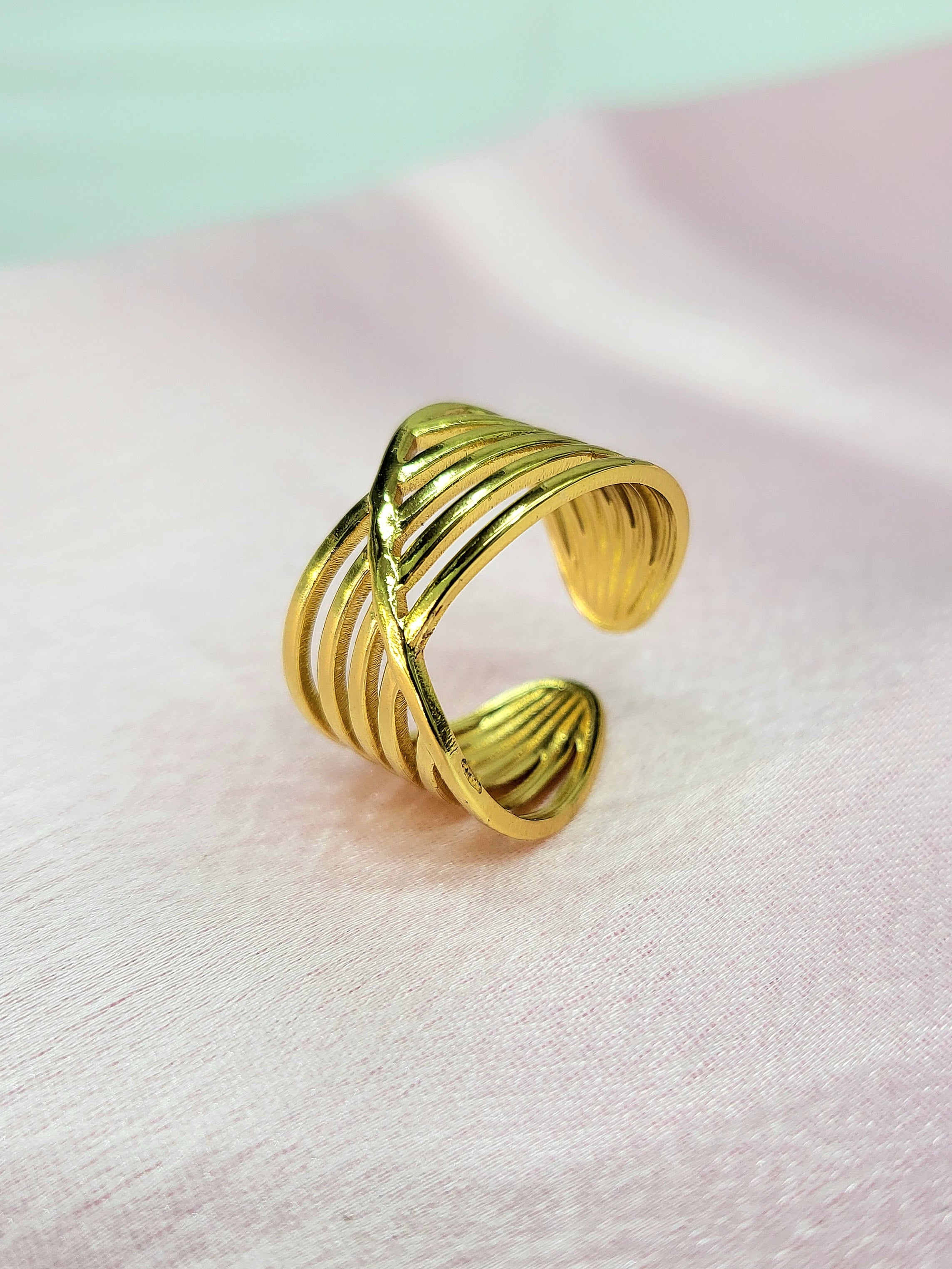 Solara adjustable anti-tarnish gold plated stainless steel wide statement ring featuring an overlapping multi-row criss-cross wire design on a soft pink background.