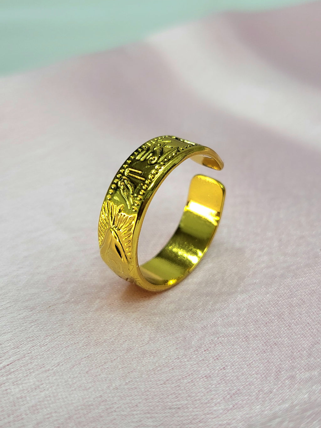 Aethra adjustable anti-tarnish gold plated stainless steel band ring featuring etched ancient Egyptian symbols including the Eye of Horus on a soft pink background.