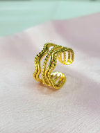 Estelle adjustable anti-tarnish gold plated stainless steel wide cage ring featuring a multi-row wave design with alternating smooth and beaded gold rows on a soft pink background.