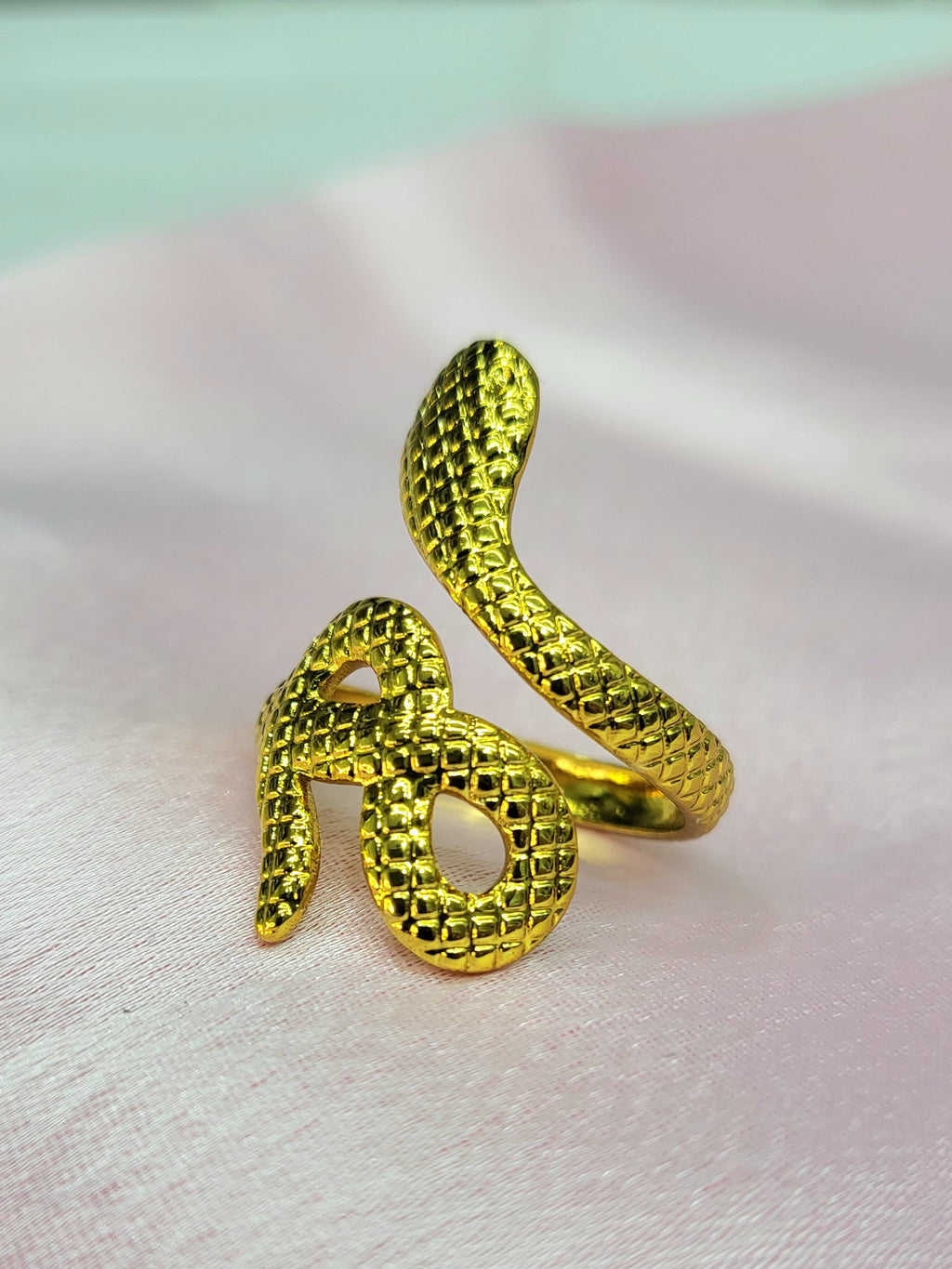 Elowen adjustable anti-tarnish gold plated stainless steel snake ring highlighting an intricate textured scale pattern on a soft pink background.