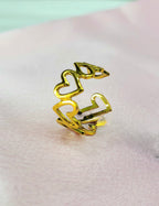 Serelith adjustable anti-tarnish gold plated stainless steel ring featuring a dainty open cut-out interlocking heart pattern on a soft pink background.