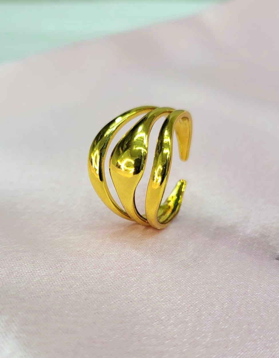 Orelia adjustable anti-tarnish gold plated stainless steel ring featuring a smooth, high-polish multi-row wave dome design on a soft pink satin background.